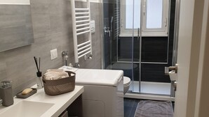 A modern bathroom with a white sink, a glass shower enclosure, and a towel rack. - Kibilù - Via Console Marcello (Milan)