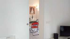Quarto com televisão, cadeira e mesa com tampo de vidro.