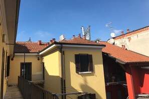 A narrow alleyway with a yellow building on the left and a red building on the right. There are multiple chimneys and satellite dishes on the rooftops. - Kibilù - Via Marghera (Milan)
