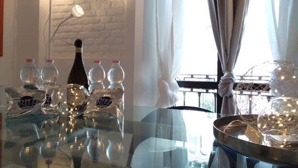 Uma mesa de vidro com garrafas e objetos decorativos, uma parede de tijolos e uma janela com cortinas.