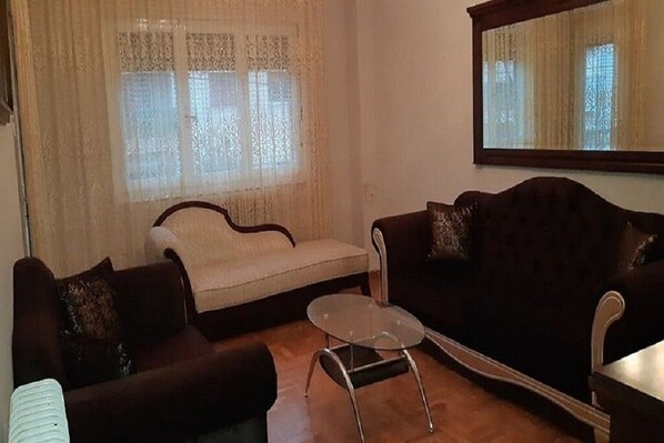 A living room with a sofa, a chair, a glass coffee table, and a window with curtains.