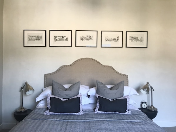 A neatly made bed with a headboard, two bedside tables with lamps, and five framed pictures on the wall.