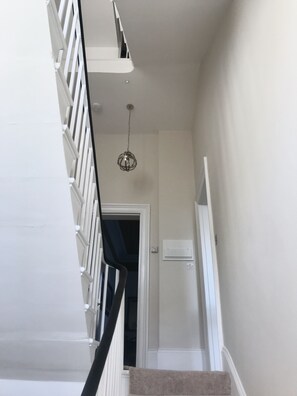 A staircase with white railings and a beige carpeted landing. A chandelier hangs from the ceiling, and an air conditioning unit is mounted on the wall. - A Beautiful Grade II regency property with parking (Cheltenham)