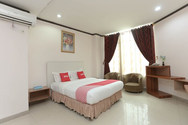 A hotel room with a bed, a chair, a wooden shelf, and a window with curtains.