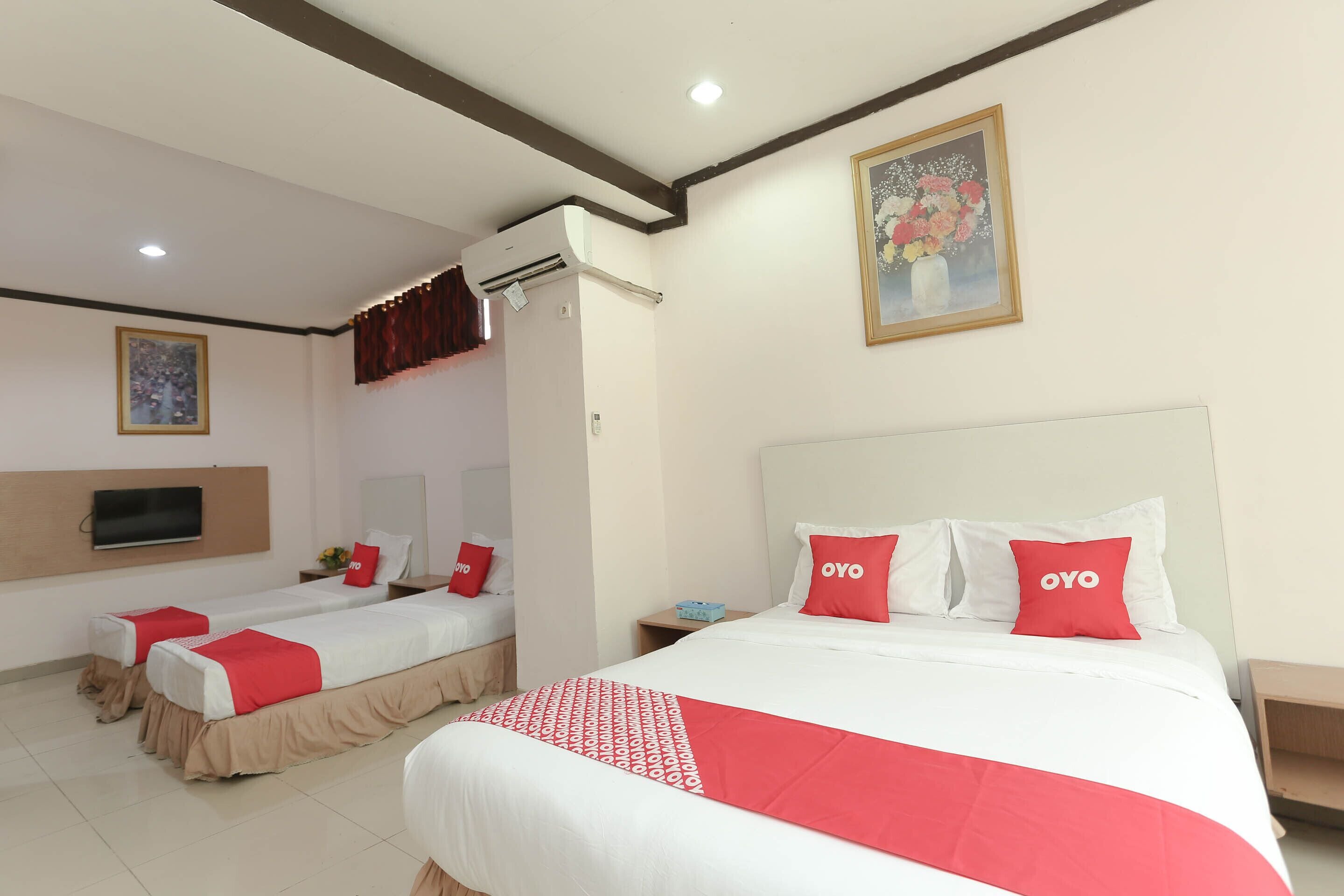 A hotel room with two beds, each with red and white bedding, a mounted TV, and a painting on the wall.