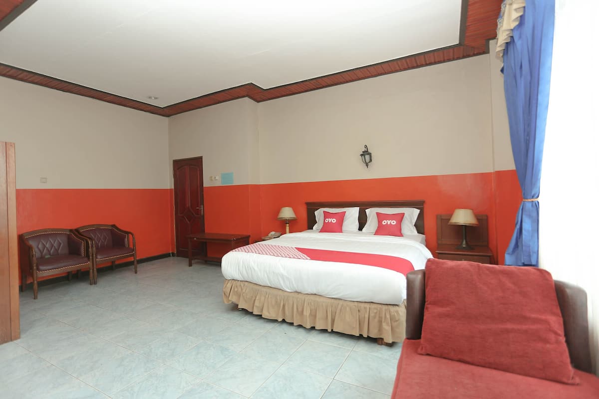 Ein Hotelzimmer mit einem Bett, zwei Holzstühlen, einem Nachttisch und einer Lampe.