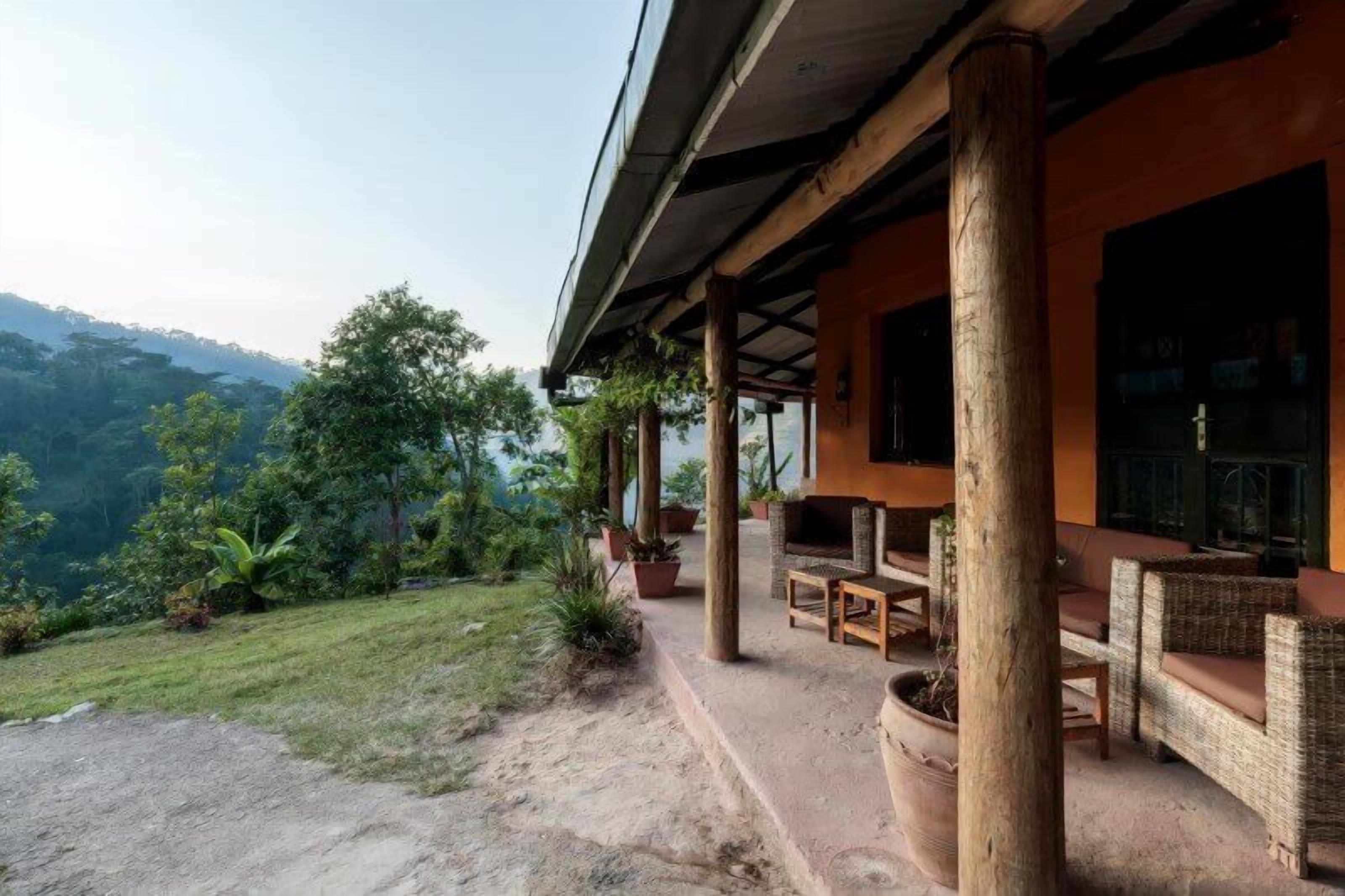 A covered outdoor seating area with wicker furniture and a stone fireplace, overlooking a lush landscape.