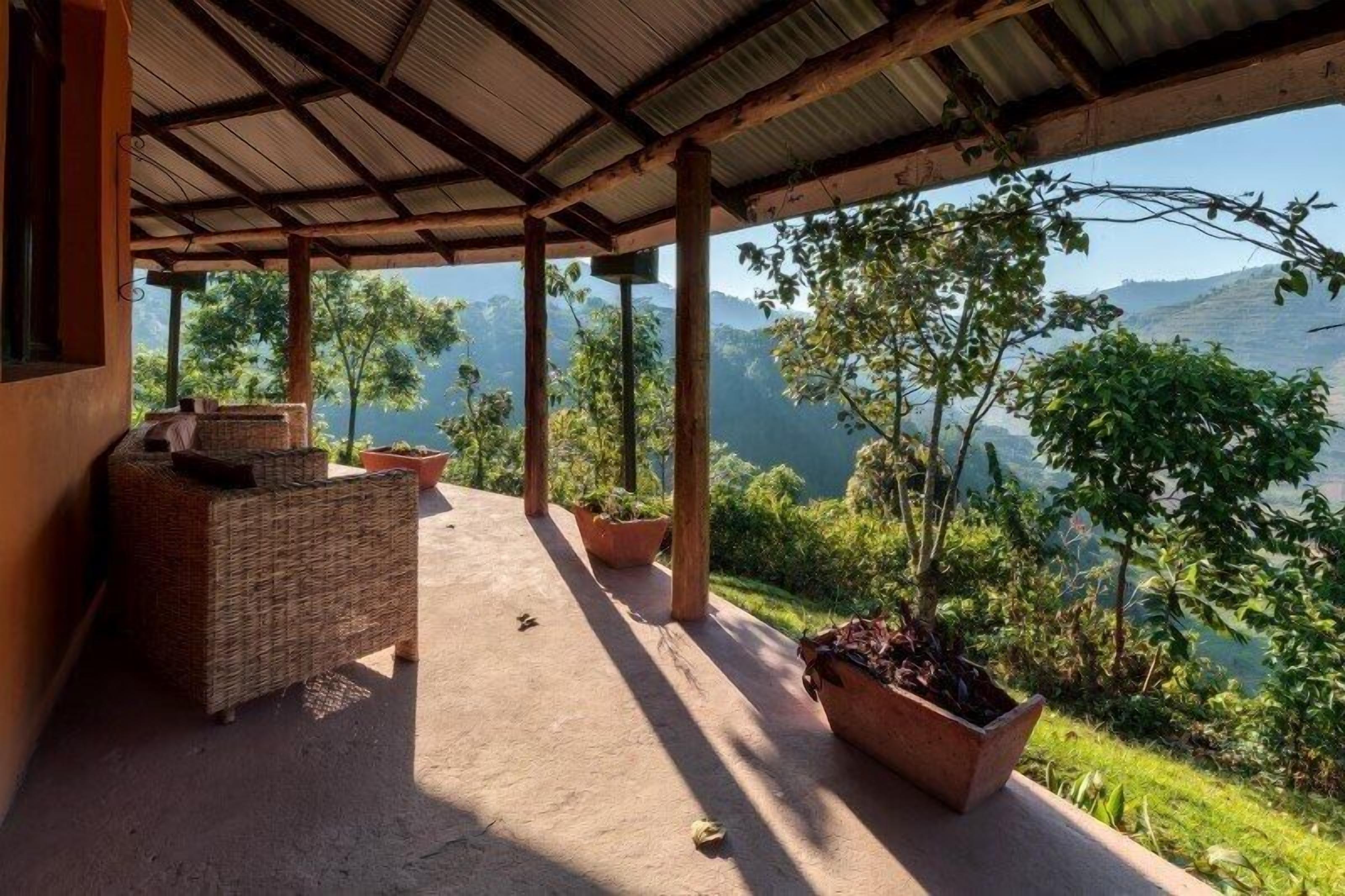 A covered outdoor area with wicker furniture and potted plants, overlooking a mountainous landscape.