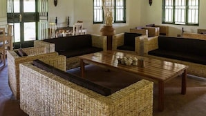 A room with wicker furniture, including sofas and a coffee table, with a large window providing natural light. - Gorilla Valley Lodge (Bwindi)