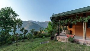 A house with a green roof, surrounded by lush greenery and a mountainous backdrop. - Gorilla Valley Lodge (Bwindi)