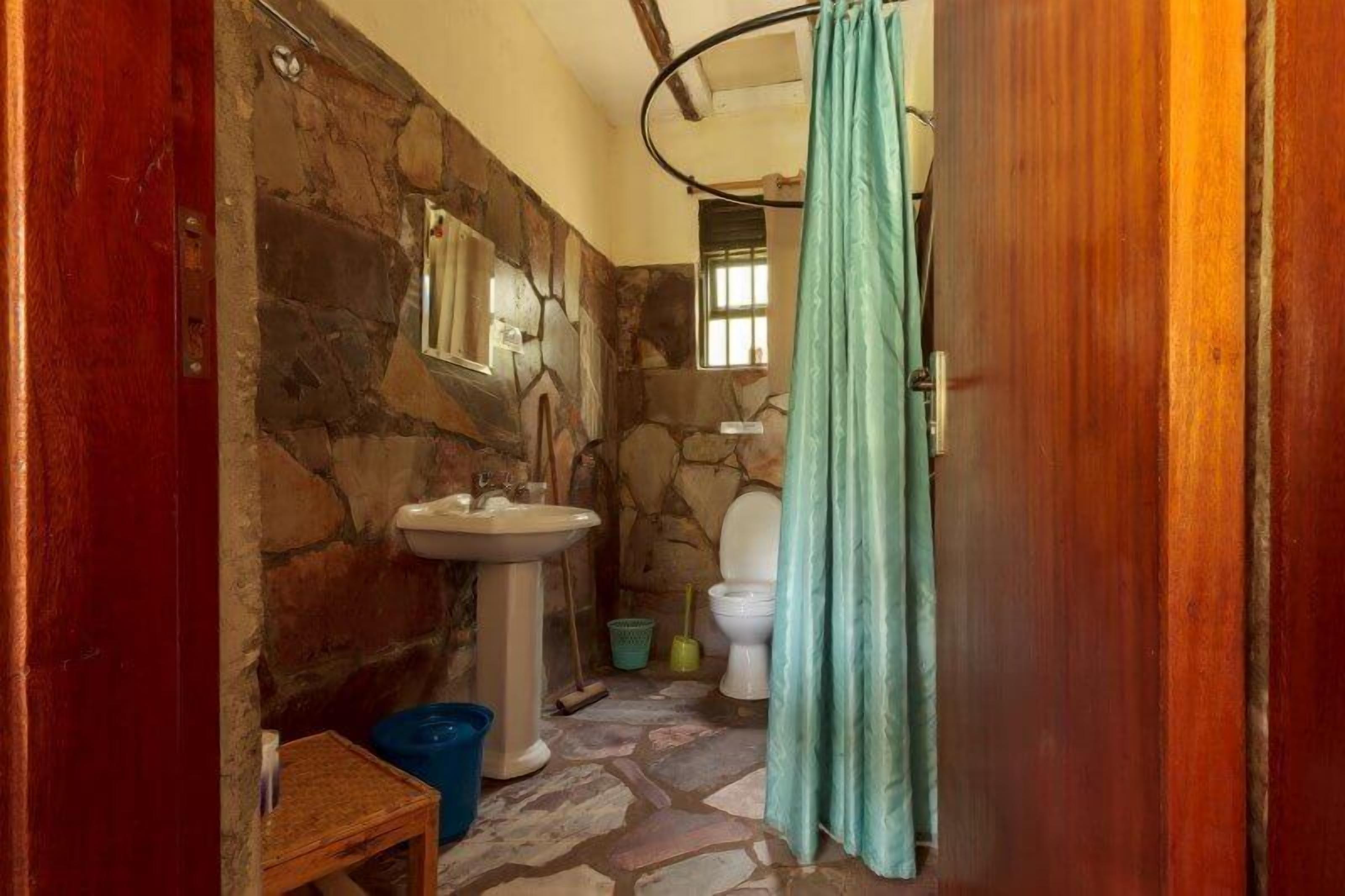 A small bathroom with a stone wall, a sink, a toilet, and a shower curtain.