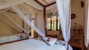 A room with a bed under a canopy, a small table, and a chair. - Gorilla Valley Lodge (Bwindi)