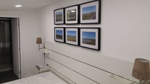 A hotel room with a bed, a bedside table, a lamp, and a wall with six framed pictures.
