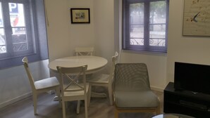 A room with a round dining table, four chairs, a television, and two windows with decorative iron railings.