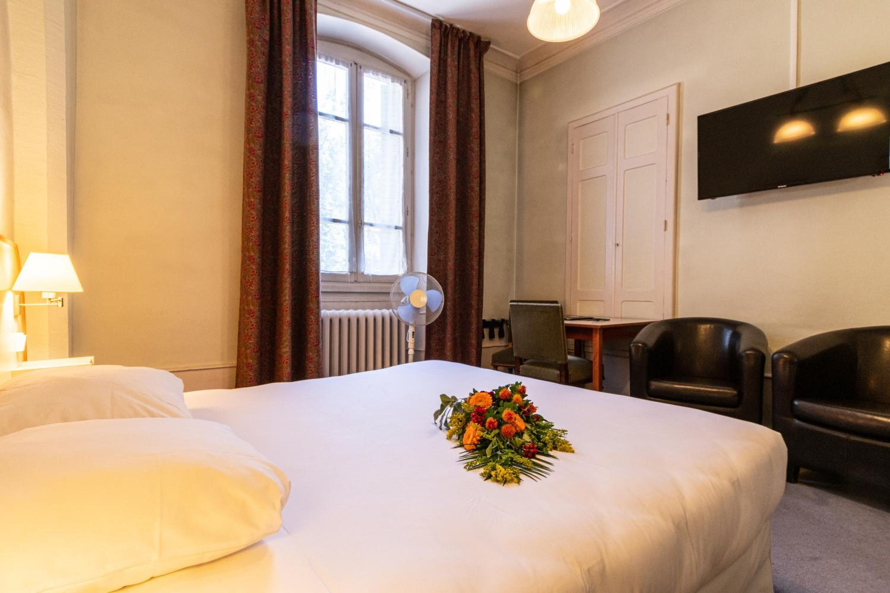 Habitación de hotel con cama, escritorio, silla, televisión y ventana con cortinas.
