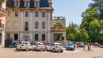 A hotel with a classic facade, a restaurant sign, and several parked cars in front.