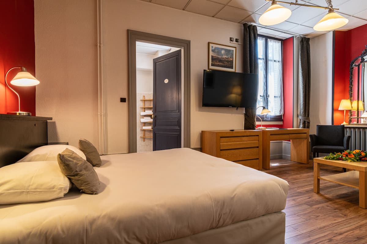 Een hotelkamer met een bed, bureau, stoel, televisie en een raam met gordijnen.