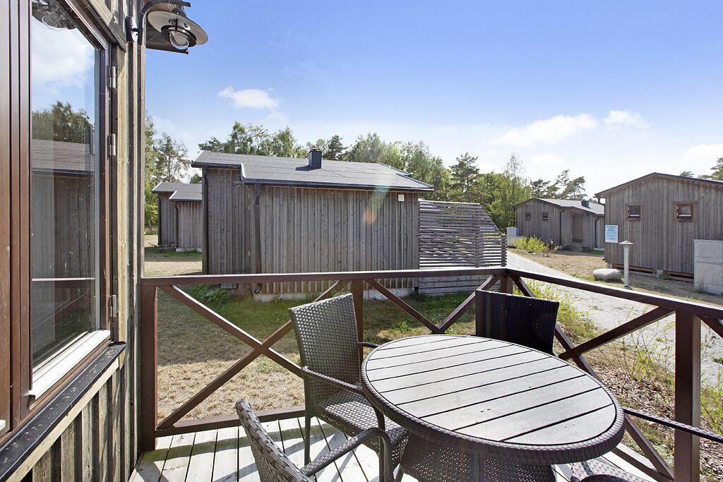 A wooden deck with a round table and chairs, surrounded by wooden buildings.