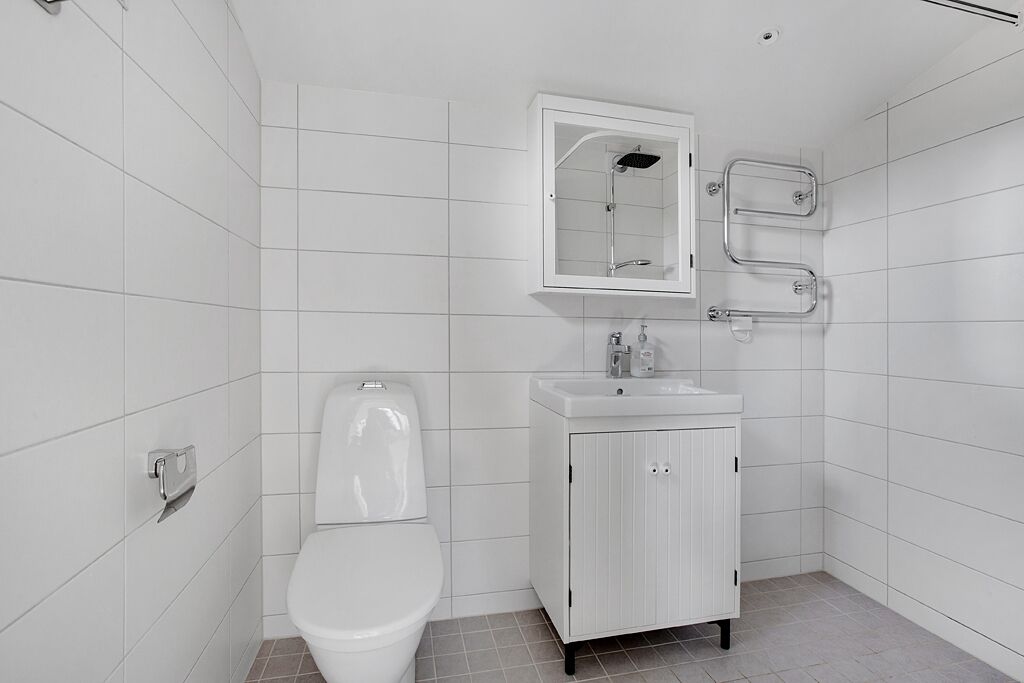 A modern bathroom with white tiles, a toilet, a sink with a mirror, and a shower.