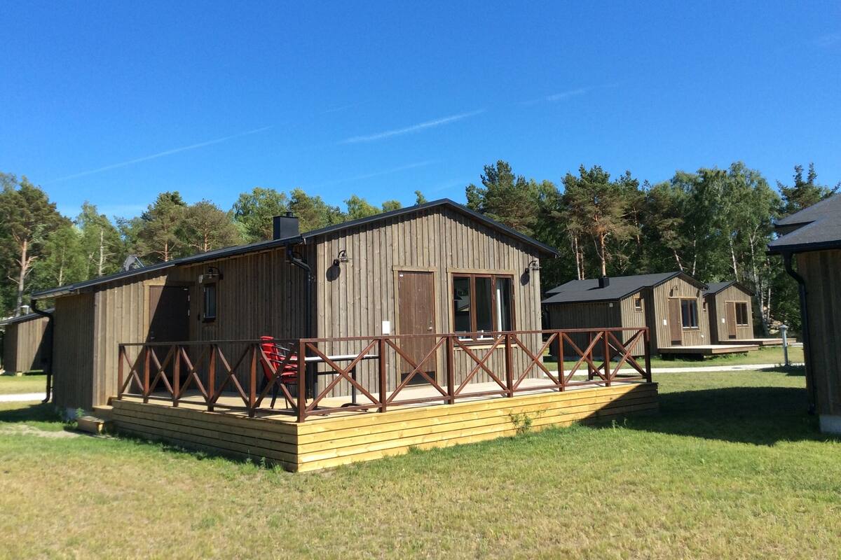 Eine Holzhütte mit einer Terrasse und einer kleinen Veranda, umgeben von Bäumen.