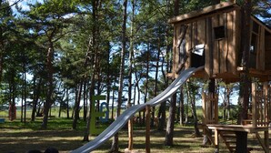 Eine Holzweltschanze mit Rutsche in einer bewaldeten Parkanlage.