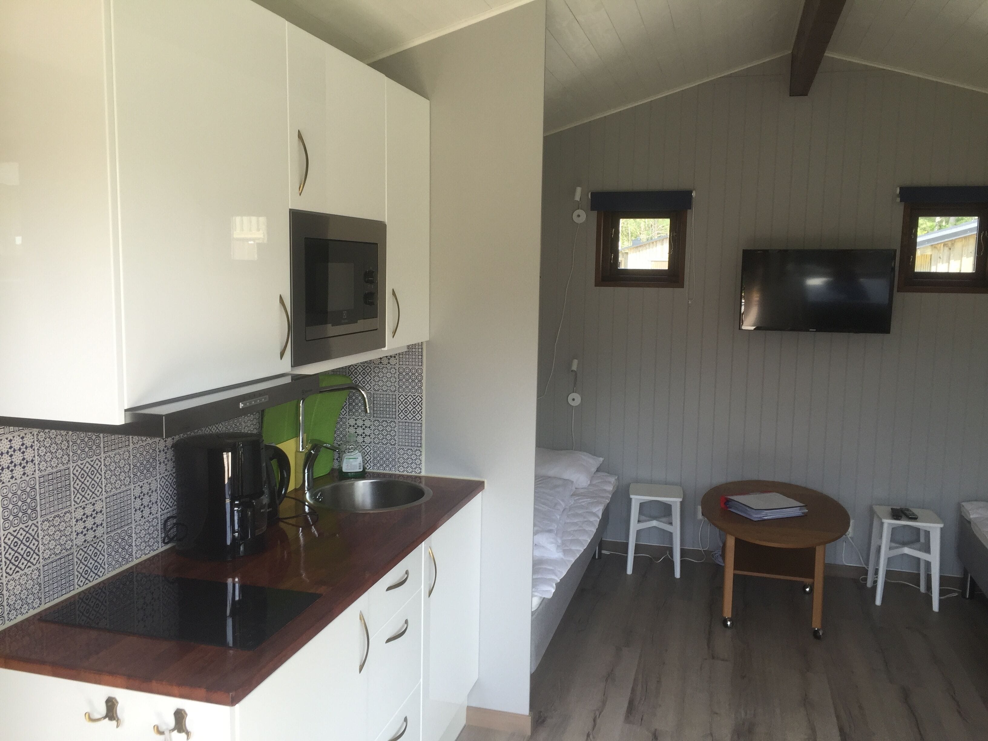 Une pièce compacte comprenant un coin cuisine, un lit, une petite table et un téléviseur fixé au mur.