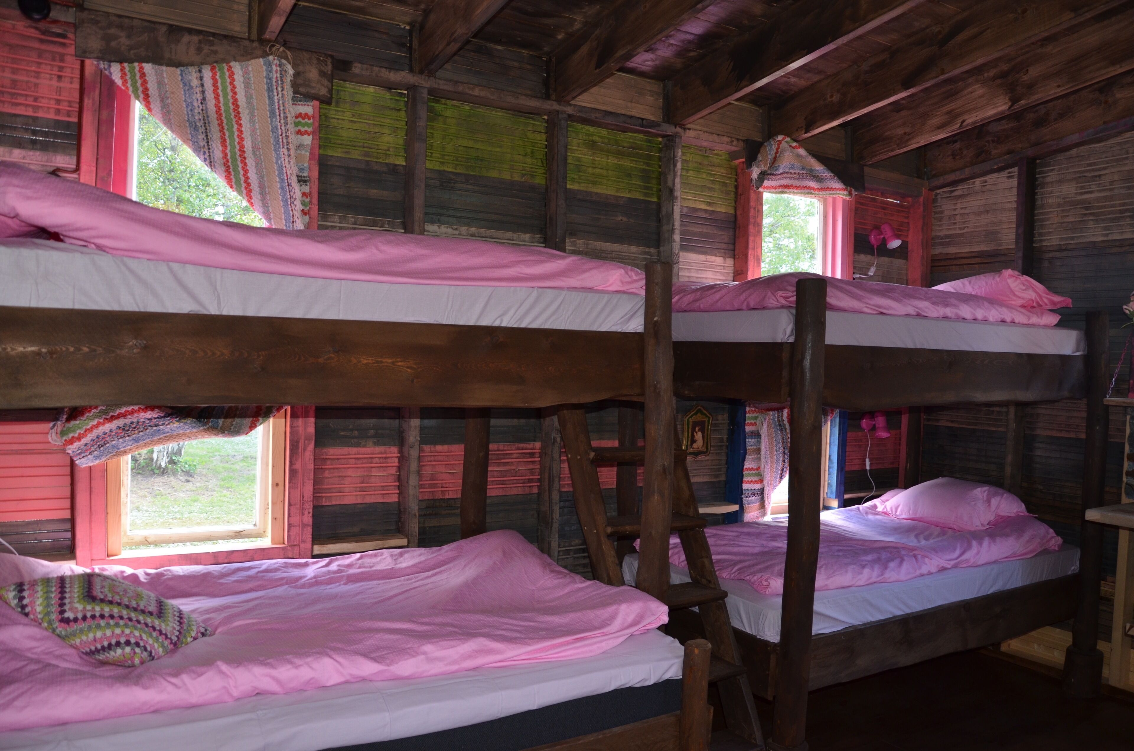 Bunk beds with pink bedding in a rustic wooden room with windows.