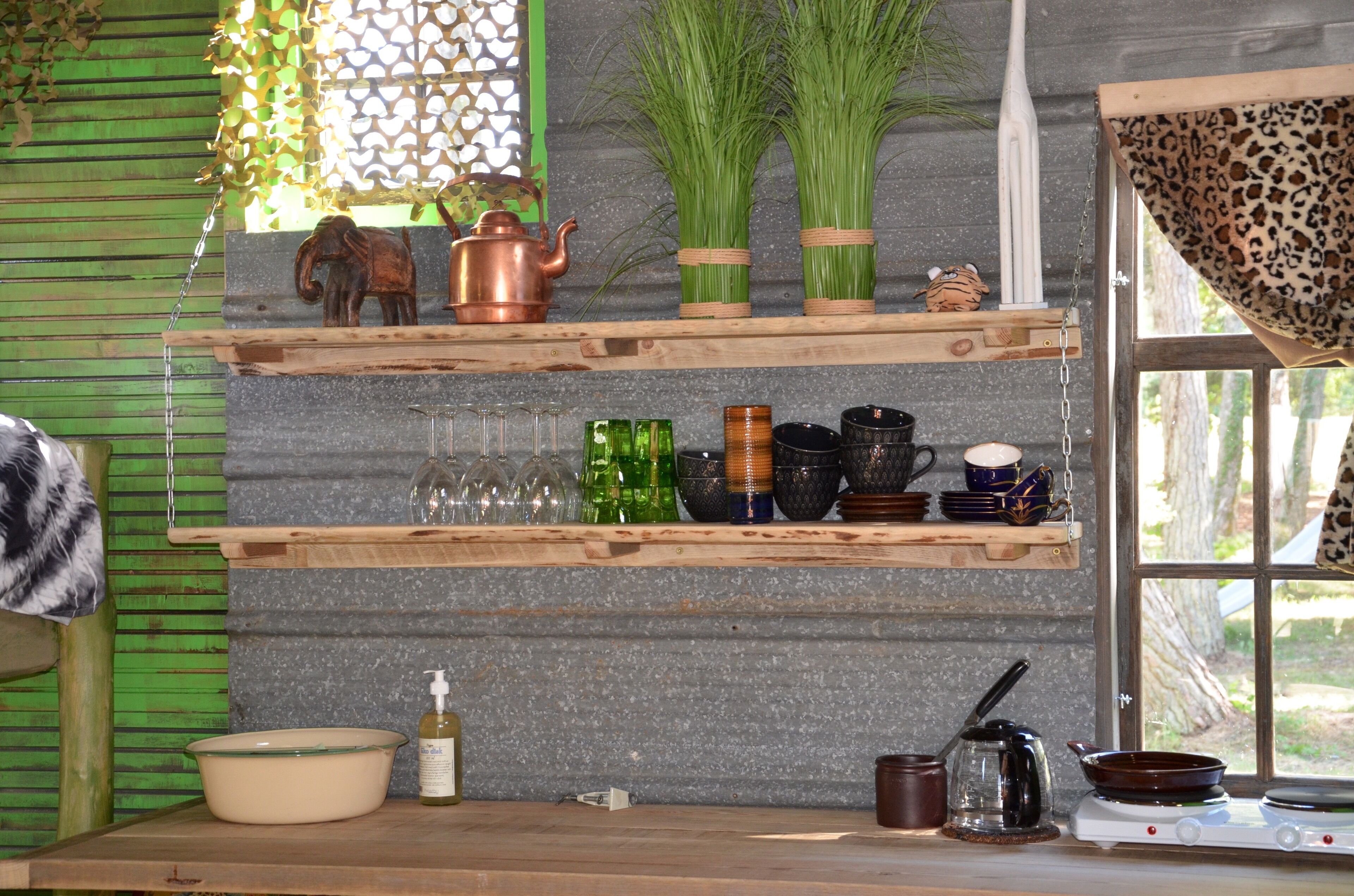 Una cocina con estantes de madera que sostienen diferentes utensilios, una estufa y una ventana con vistas.