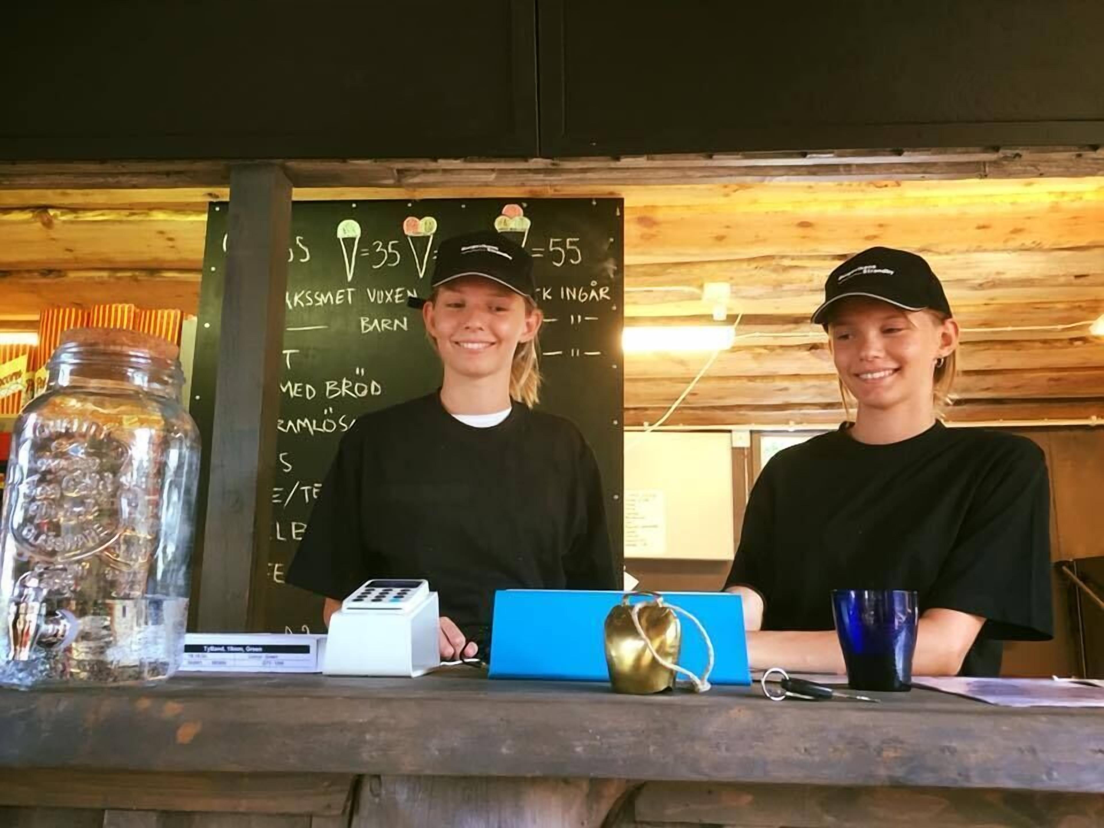 Two individuals at a counter with a chalkboard menu in the background.