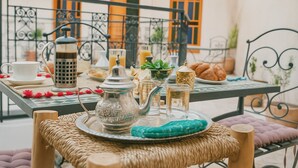 Una mesa dispuesta con tetera, tazas y pastelería, con vistas a un balcón al fondo.