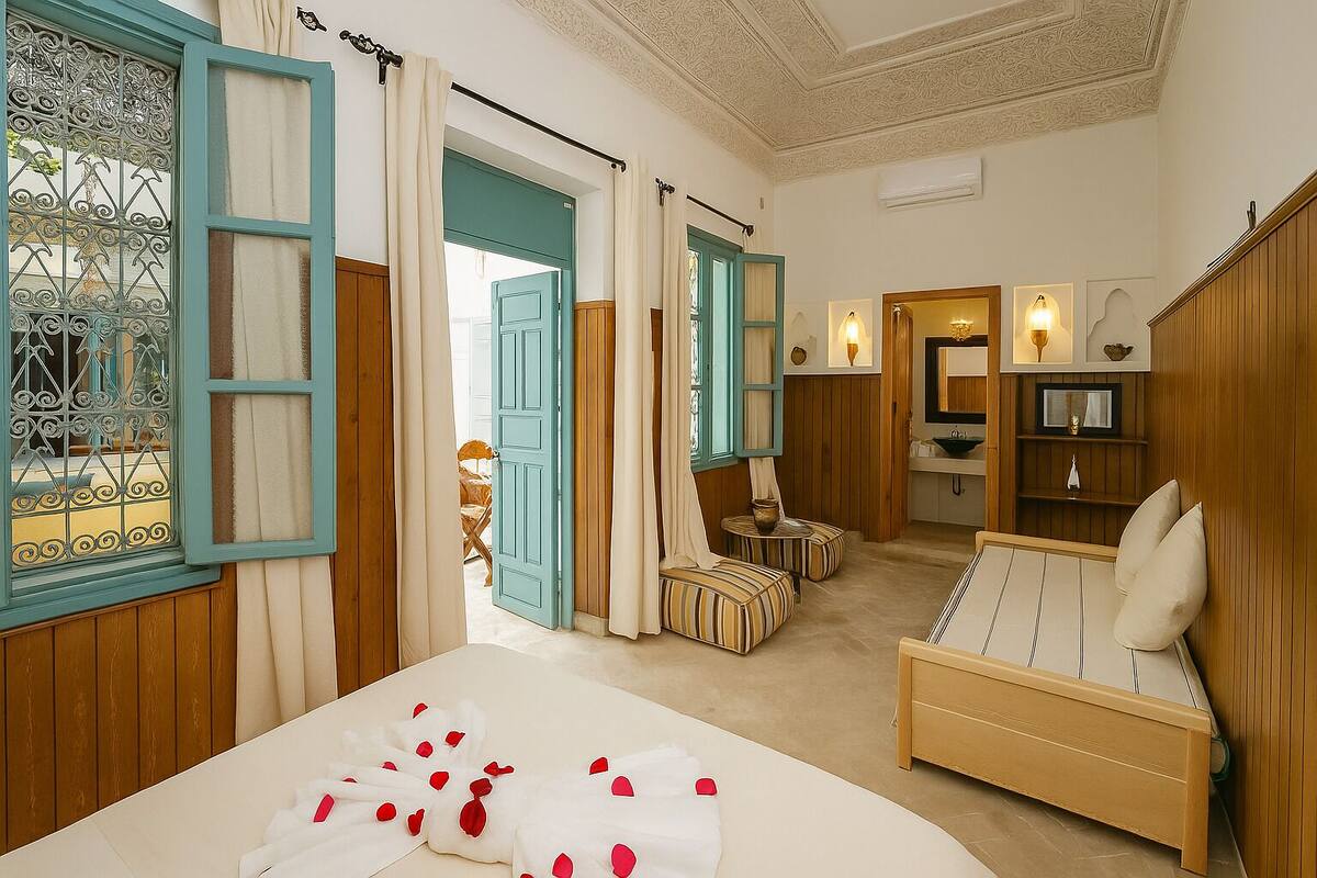 Un dormitorio con cama, sofá, una mesita y un baño visible a través de una puerta abierta.