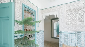 Una habitación con intrincados diseños de baldosas blancas y azules, una planta grande en maceta y un umbral que conduce a otra estancia.