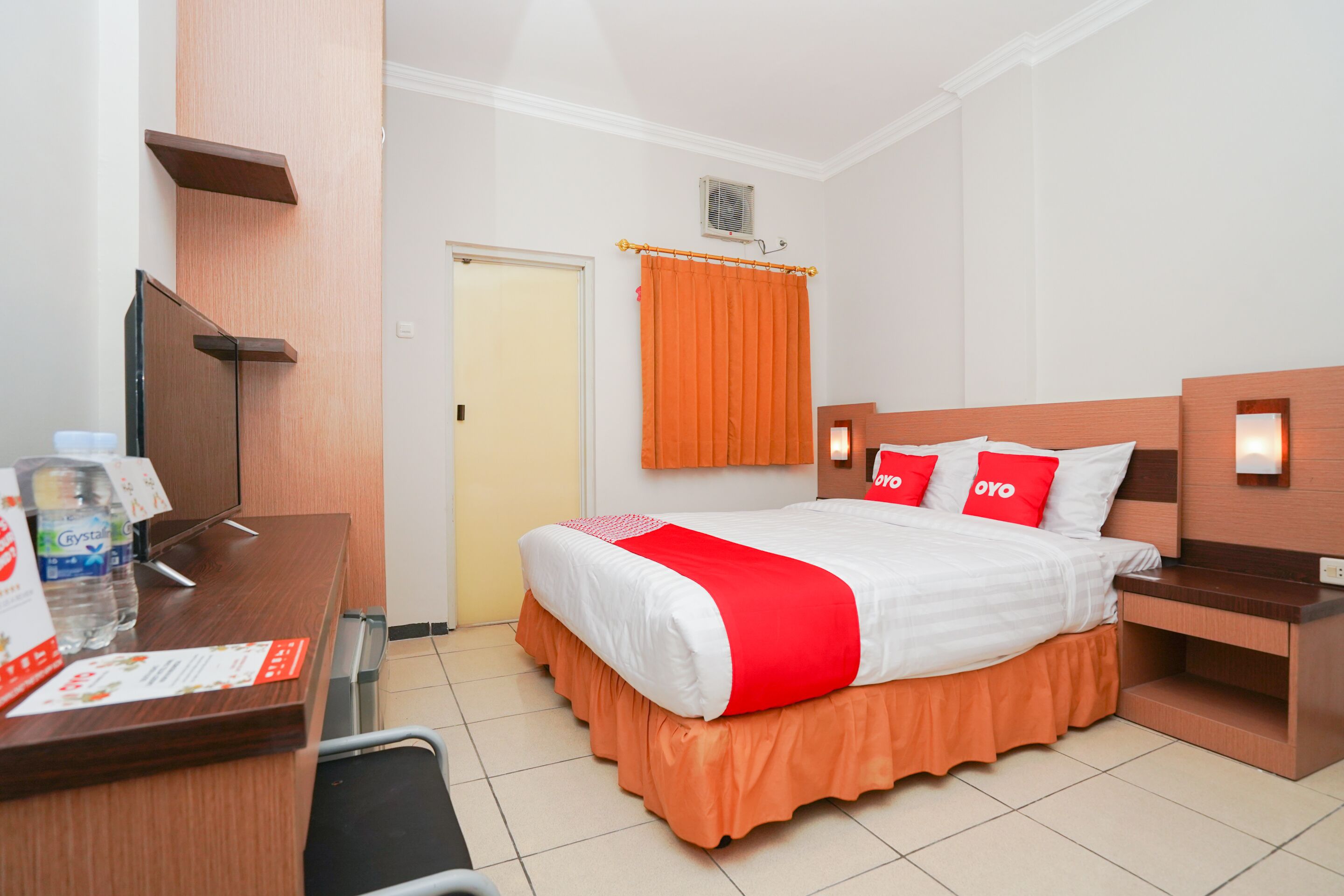 Une chambre d’hôtel avec un lit, un bureau avec un ordinateur, une chaise, une télévision et une porte.