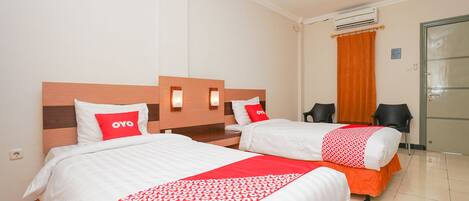 A hotel room with two beds, each with white bedding and red accents, a wooden headboard, and an air conditioning unit on the wall.