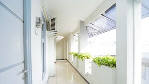 A corridor with white walls, tiled floor, and a window with a blue awning. - Hotel O Graha Marina (Surabaya)