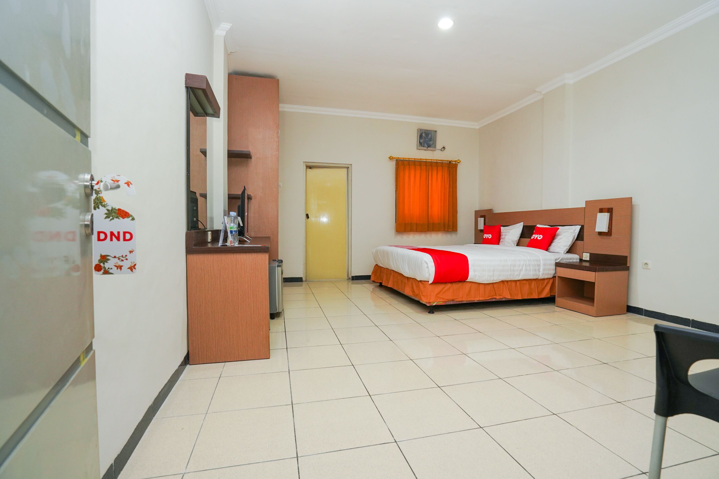 Une chambre d’hôtel avec un lit, un bureau, une chaise, une porte et une fenêtre avec des rideaux.