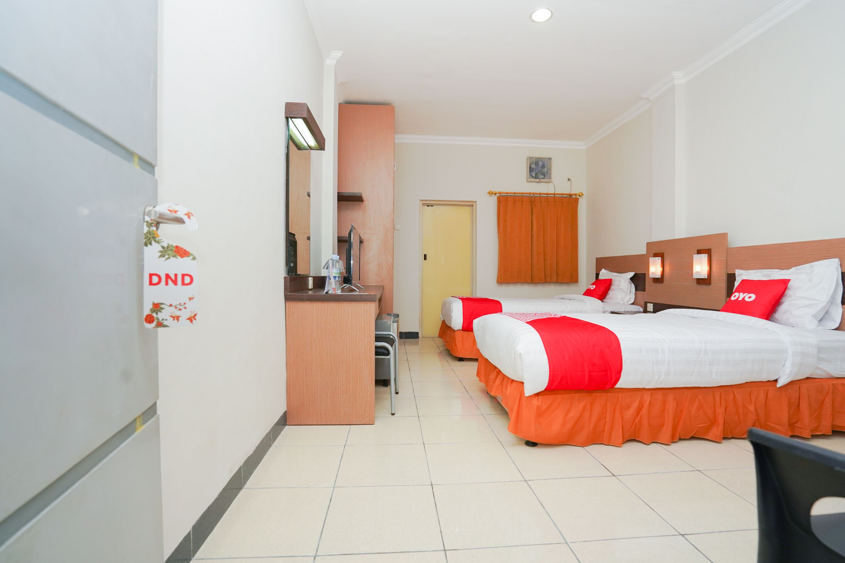 A hotel room with two beds, a desk, a chair, and a bathroom.