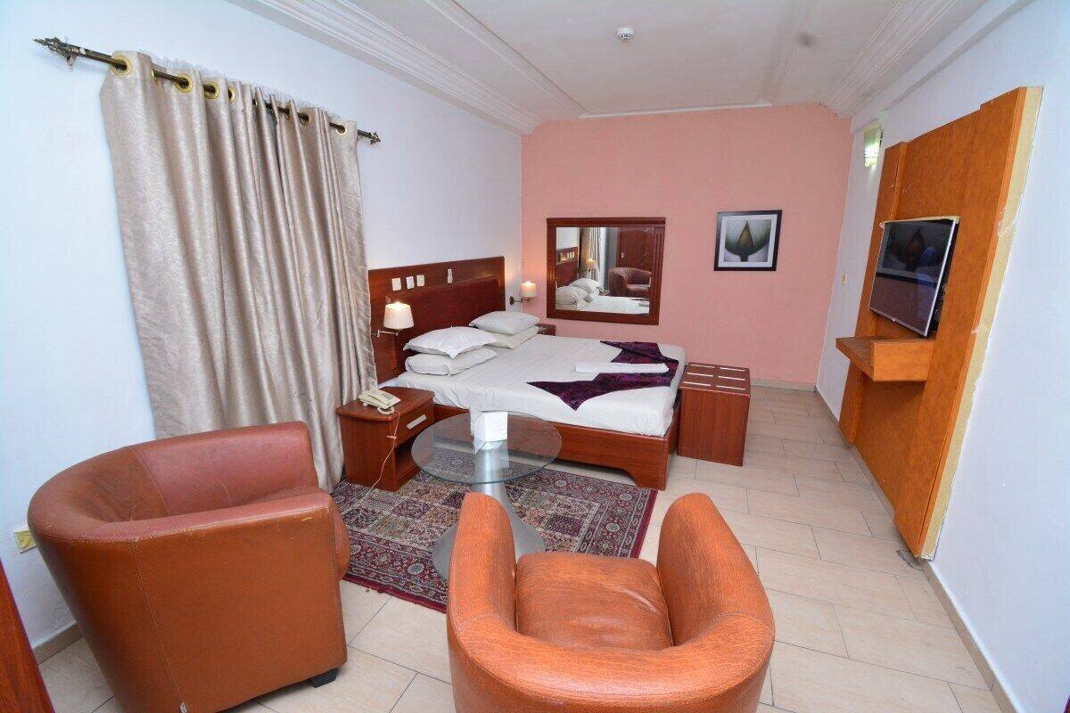 A hotel room with a bed, two chairs, a bedside table, a mirror, and a TV.