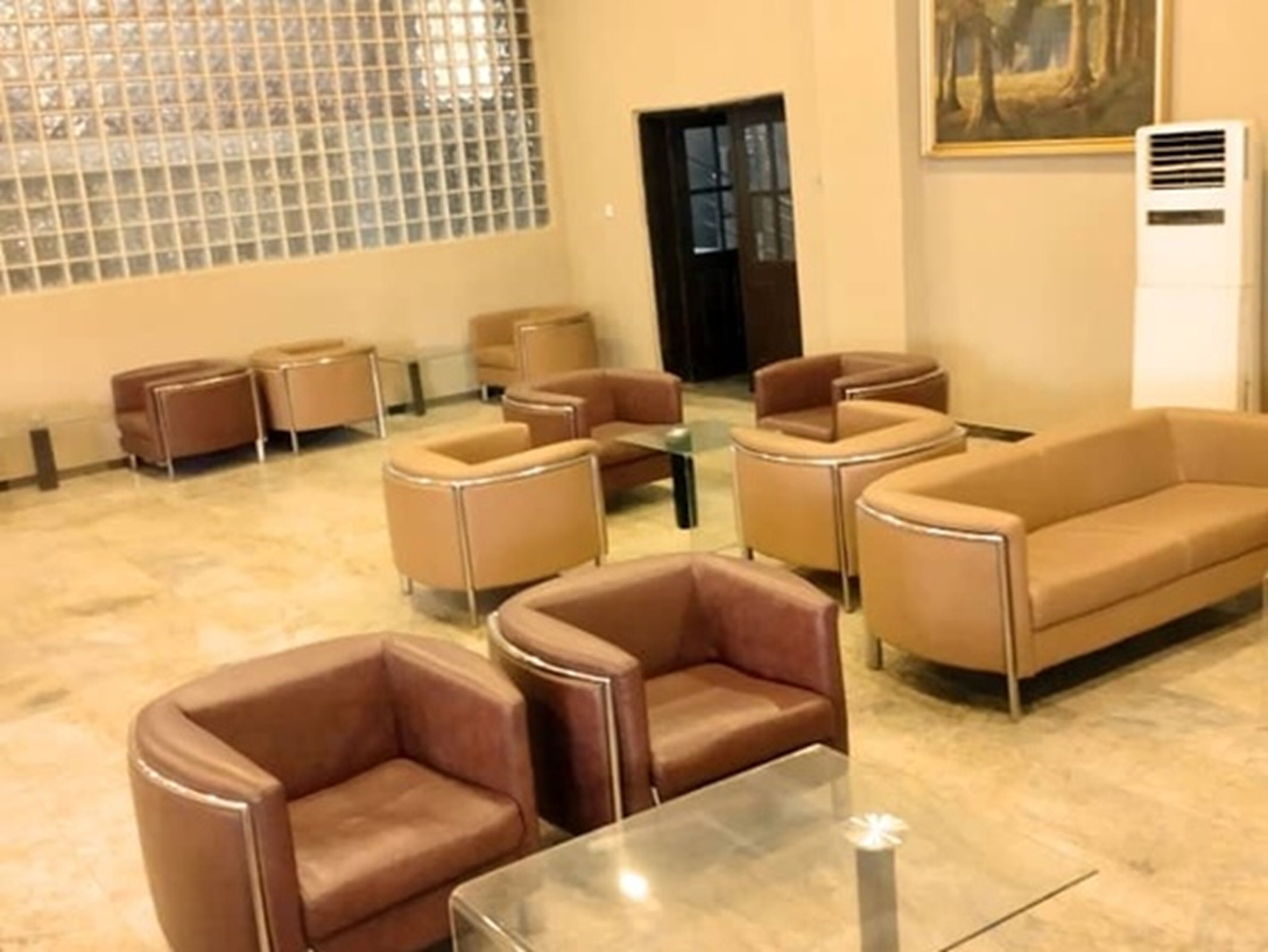 A lobby with leather sofas and armchairs, a glass coffee table, and a painting on the wall.