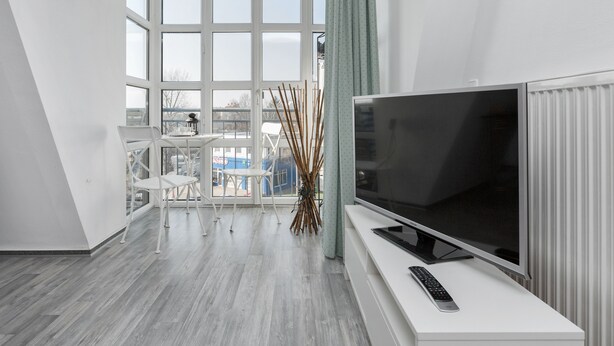Una sala moderna con un televisor de pantalla plana grande, un sofá blanco y una mesa de comedor con sillas.