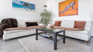 Una sala de estar moderna con un sofá blanco, una mesa de centro oscura y un cuadro grande de una playa.
