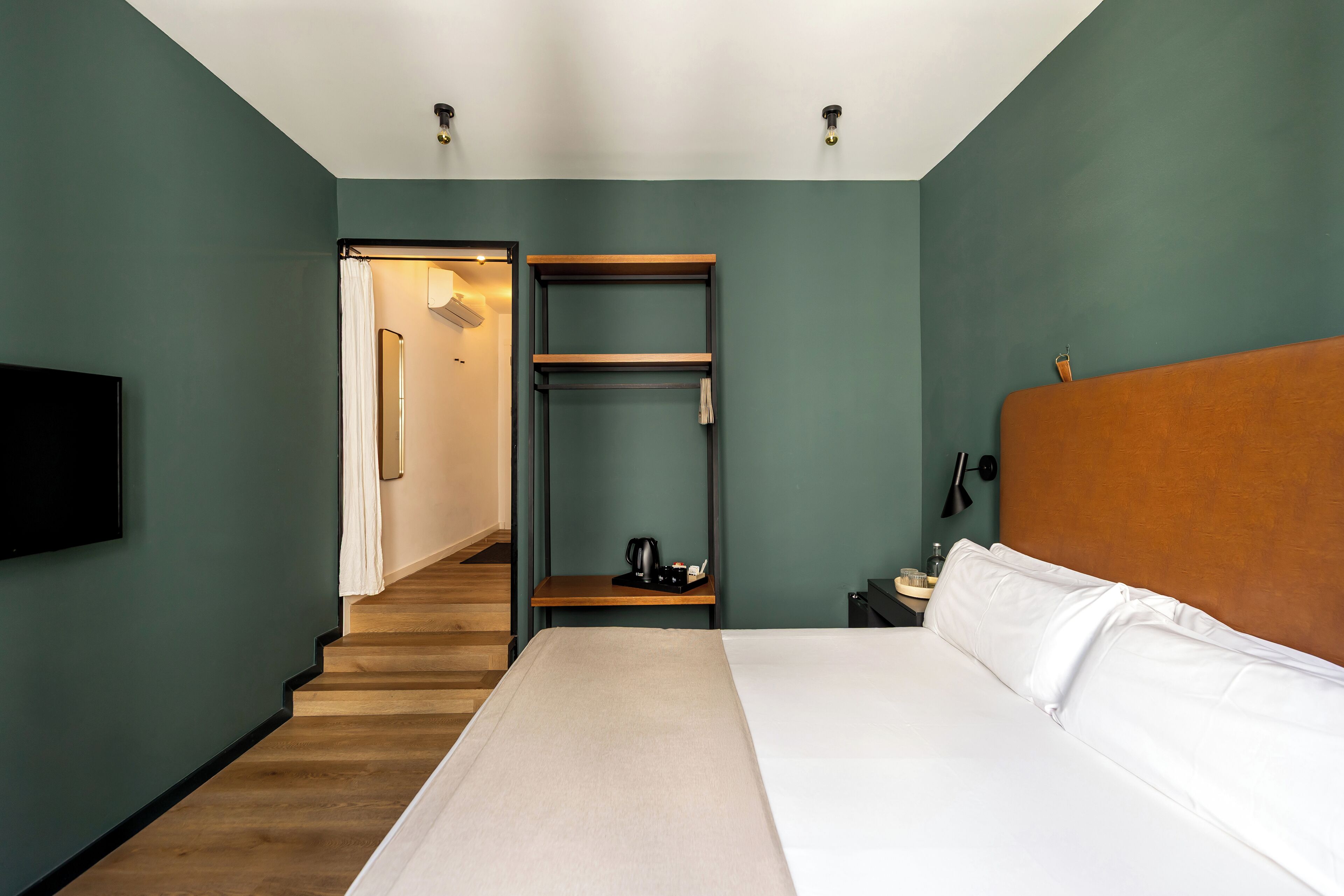 A hotel room with a bed, a TV, a nightstand, a shelf, and a staircase leading to another room.