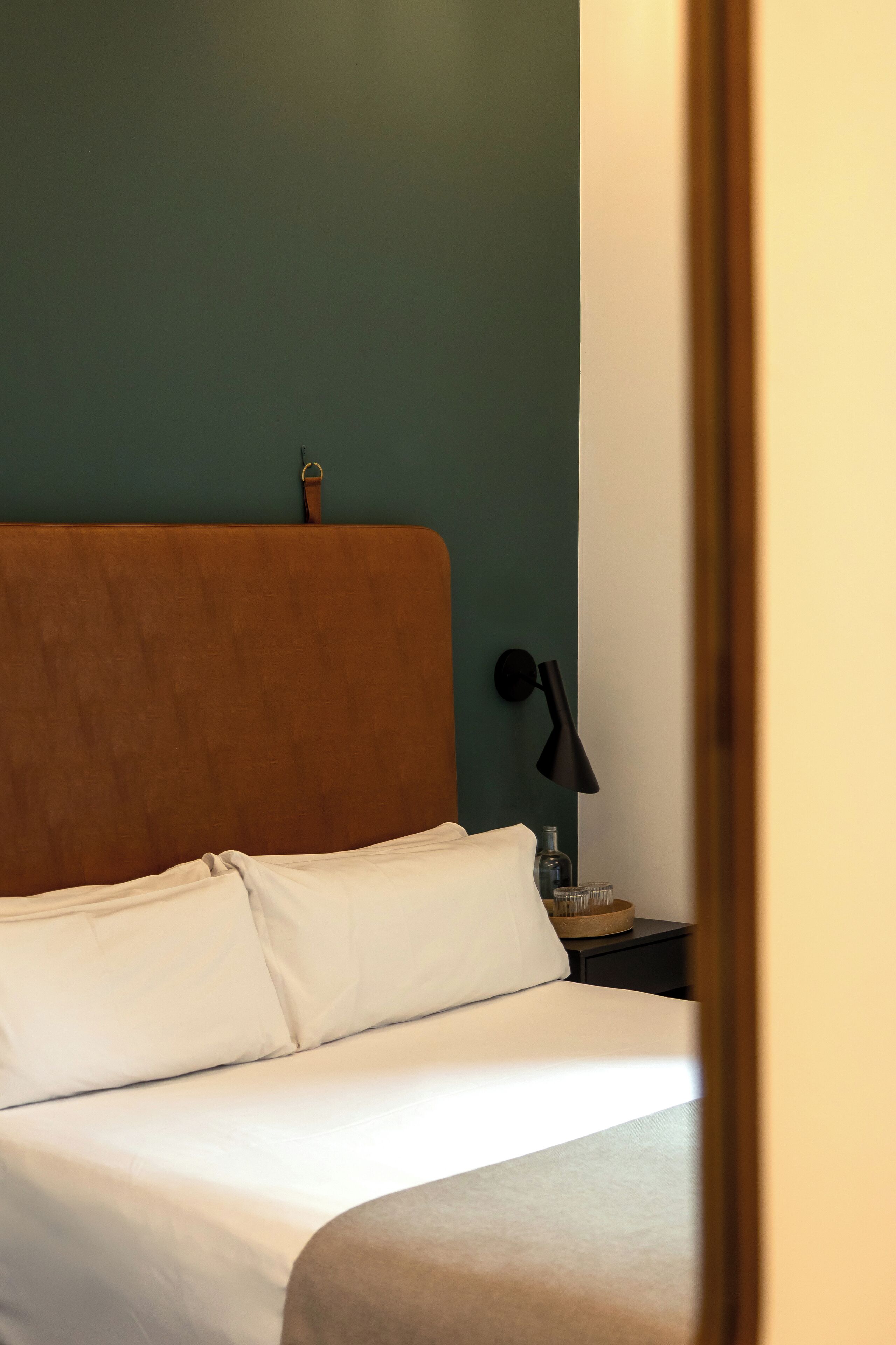 A neatly made bed with white linens, a wooden headboard, and a small bedside table with a lamp.