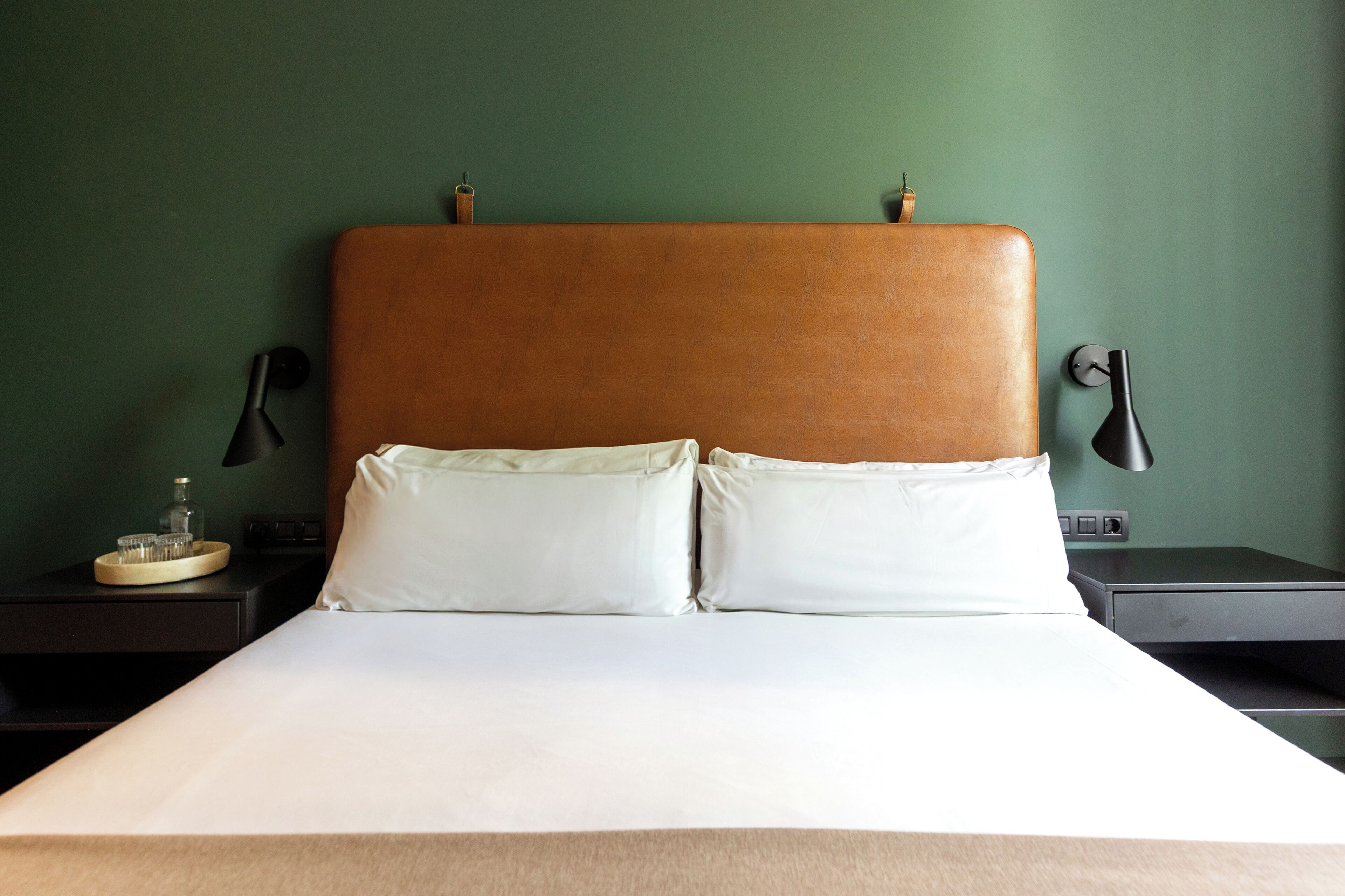 A hotel room with a large bed, two pillows, a wooden headboard, bedside tables, and a green wall.