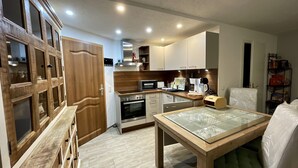 A compact kitchen with wooden cabinets, a microwave, a coffee maker, and a dining table with a green cushion. - Ferienwohnung Romance (Ebersbach)