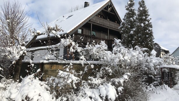 A wooden chalet with a steep roof, a balcony, and snow-covered surroundings. - Ferienwohnung Romance (Ebersbach)