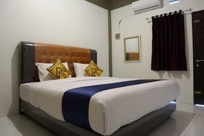 Een netjes opgemaakt bed met blauwe accenten, een bruin hoofdbord en twee gele kussens met zwarte patronen.