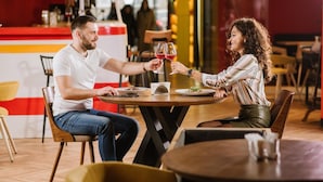 A couple toasting with wine glasses at a round table in a restaurant with wooden chairs and a red and white striped counter. - !FEST Hotel Lemkivska (Lviv)