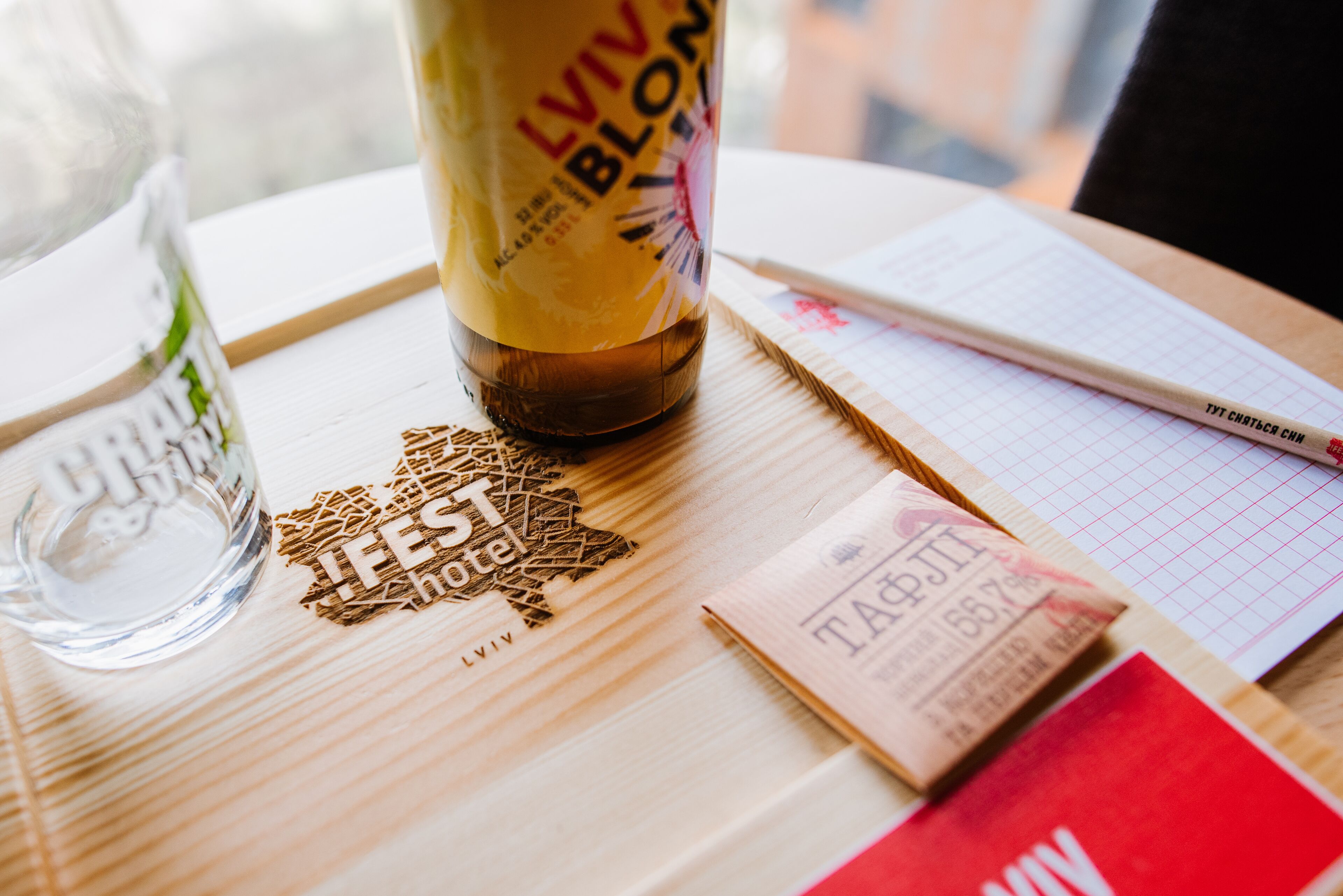 A wooden table with a bottle of Lviv Blonde beer, a glass of water, a notebook, and a red card.