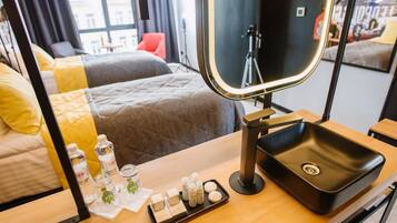 Ein Hotelzimmer mit einem Bett, einem Schminktisch mit Spiegel, einem Waschbecken und Pflegeprodukten auf der Ablagefläche.